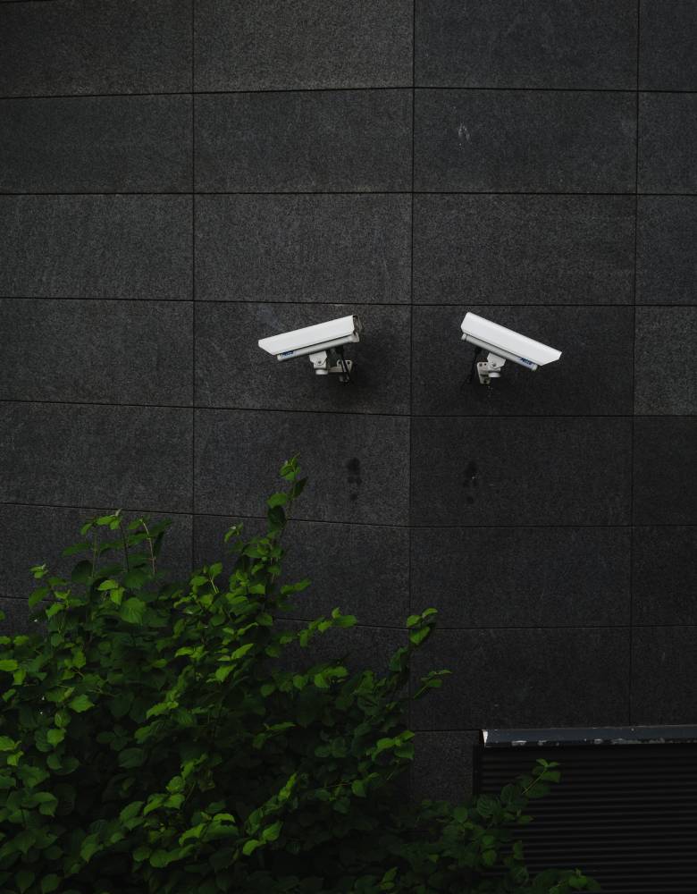 Two white CCTV cameras attached to a blank wall outside.