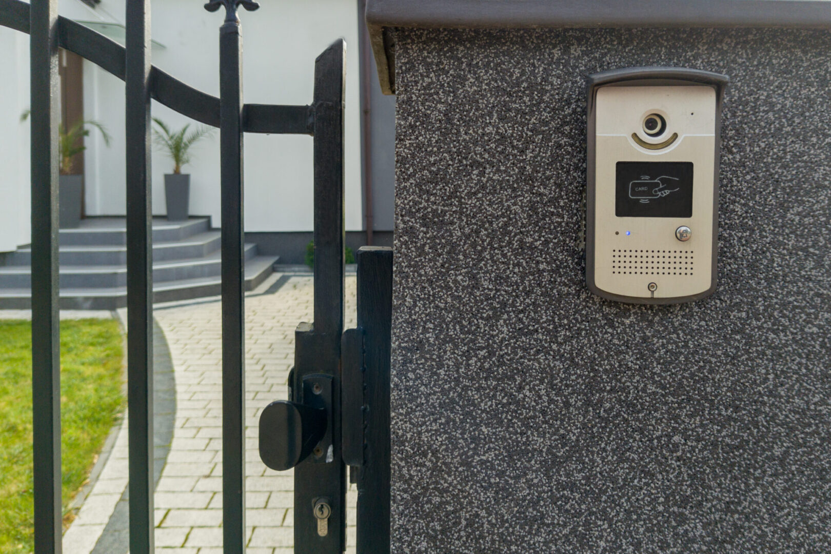 Close up of a black metal gate with a card access intercom and key lock system installed on a textured wall